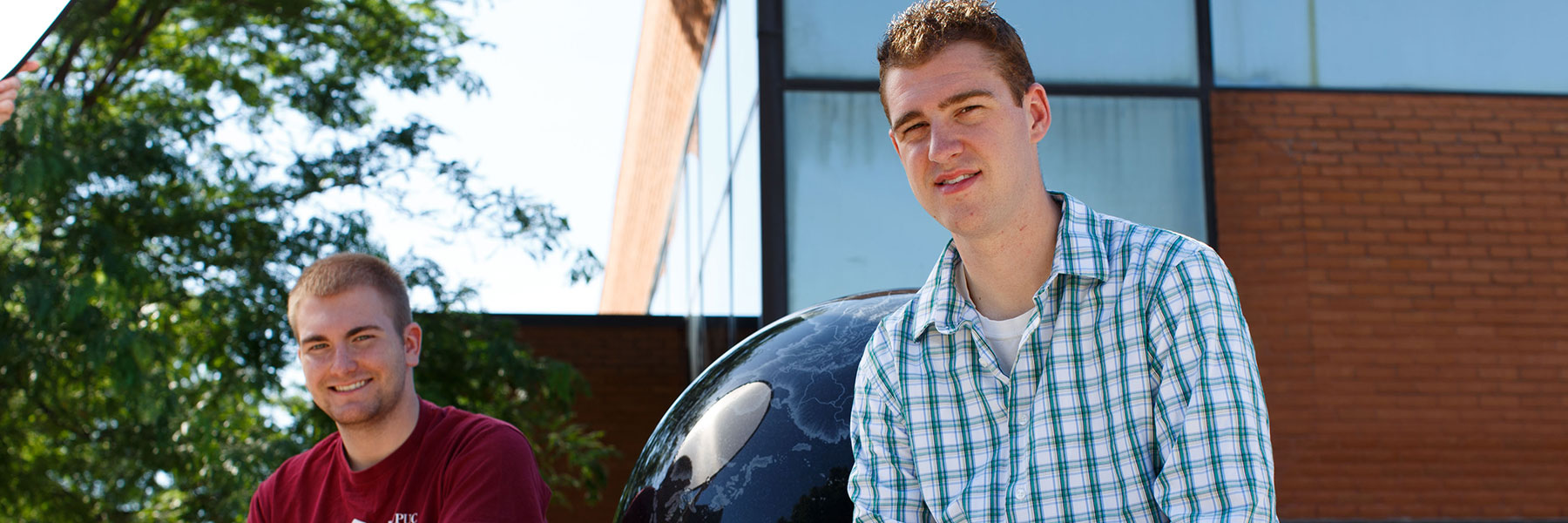 Photo of two male students sitting beside the discovery globe statue.