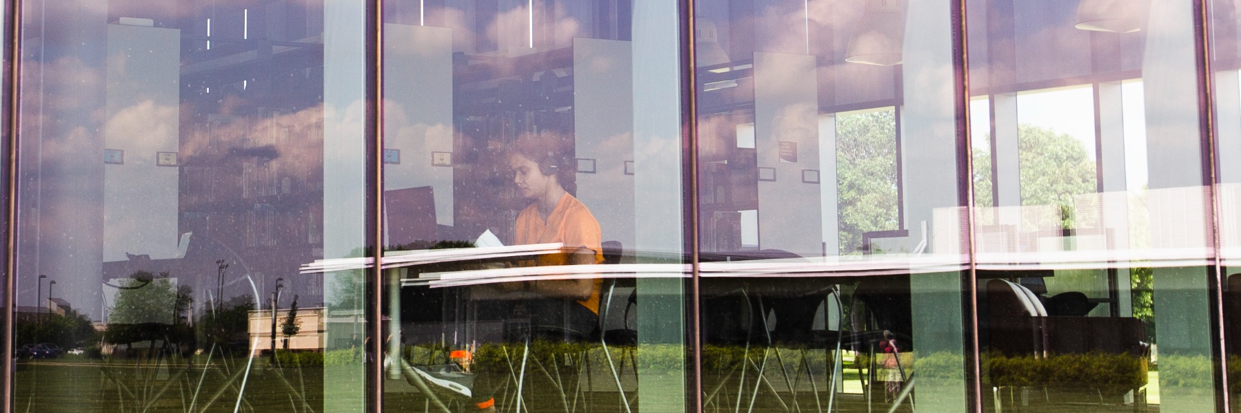 Photo of a student studying in the library taken through a window outside the library.