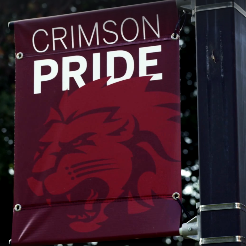 Vibrant 'Crimson Pride' banner proudly displayed, featuring the university logo and colors against a clear blue sky backdrop.